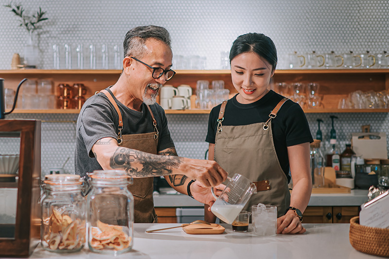 A tattooed barista teaches another barista