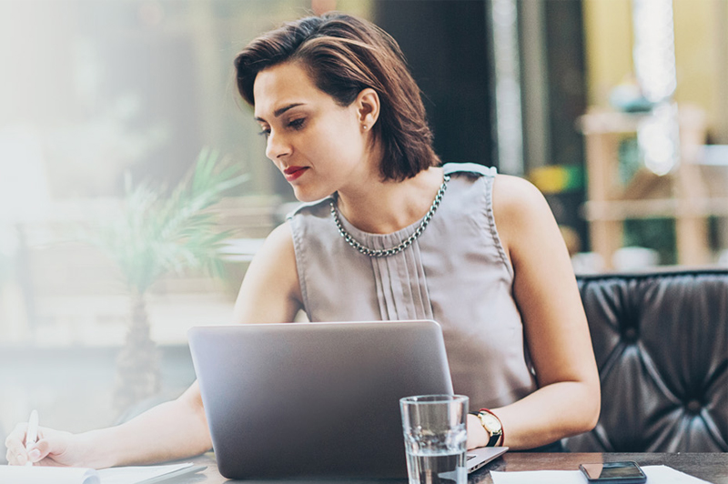 A woman writes something down while in front of her laptop