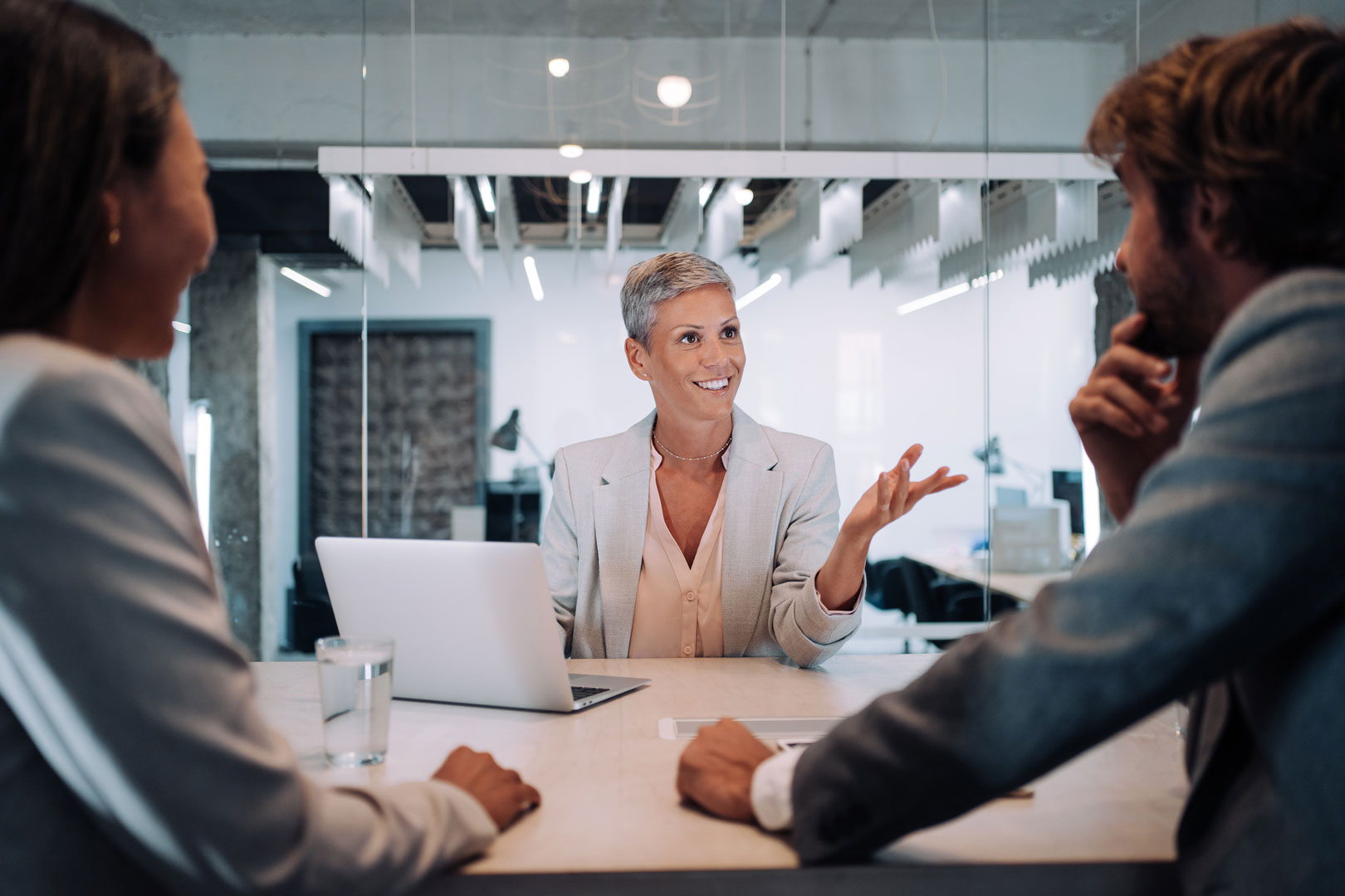 An older woman with short hair speaks to two business people at a table