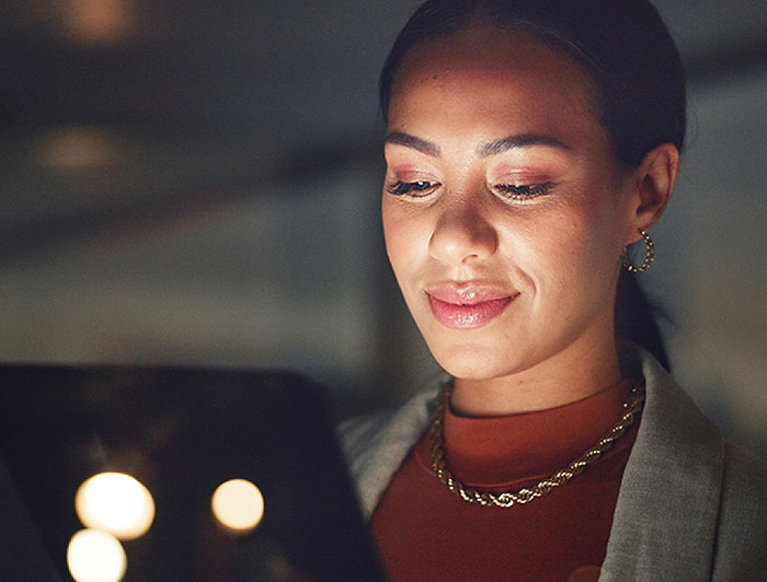 A woman looks at a tablet in a dark room, the screen illuminates her face
