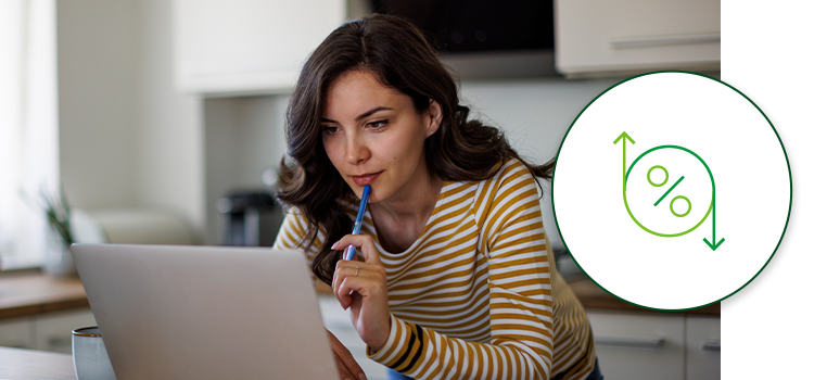 A woman looks her laptop in her kitchen with a pen to her lips