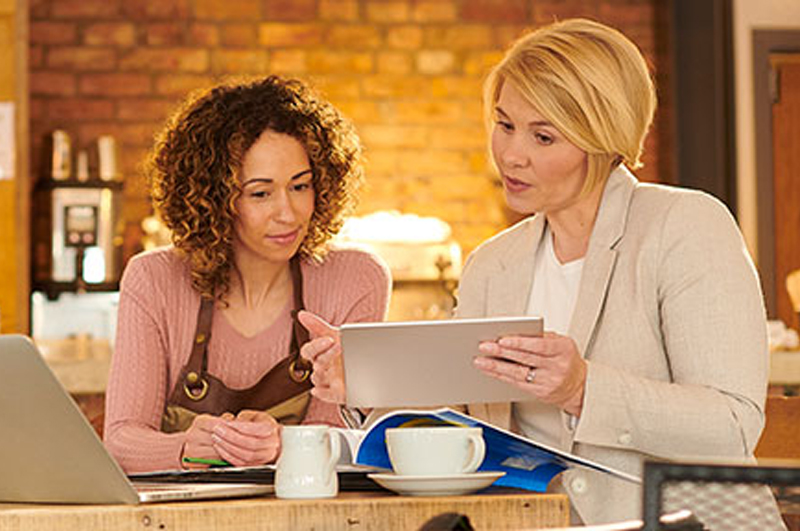 A barista speaks to a business woman holding a tablet