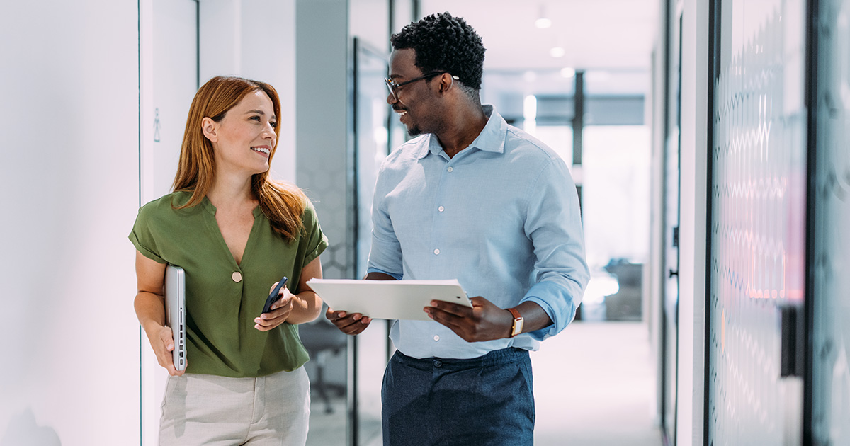 Two colleagues walk down an office hallway together
