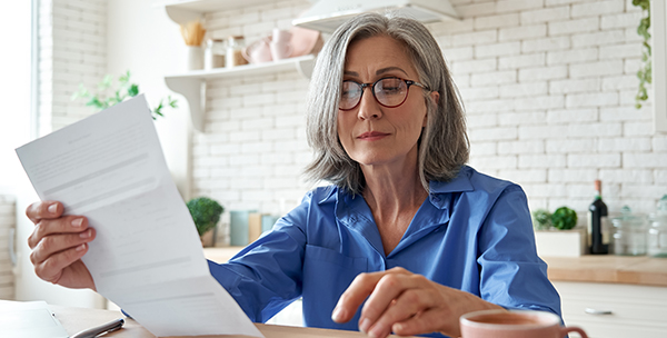 An older woman with glasses looks at a document at her kitchen table