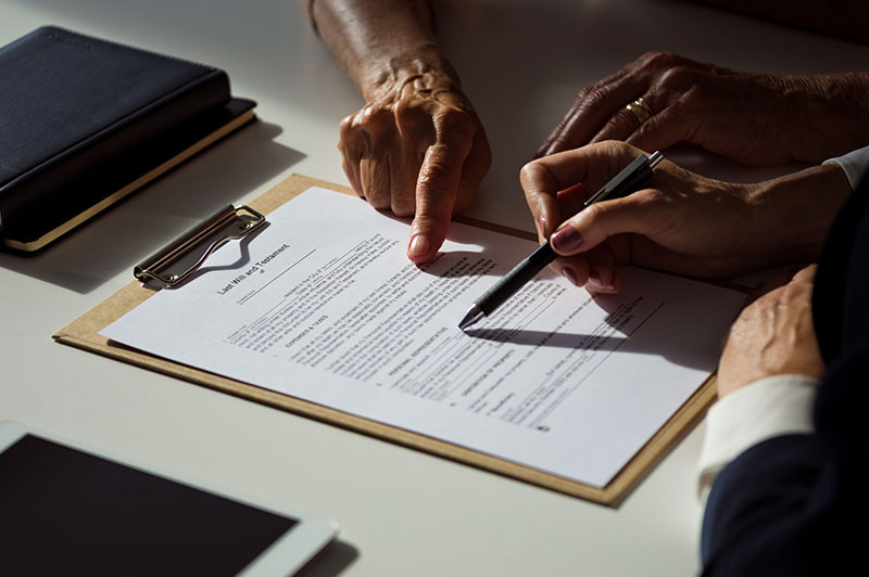 A pair of hands guides another pair of hands to the signature area of a document