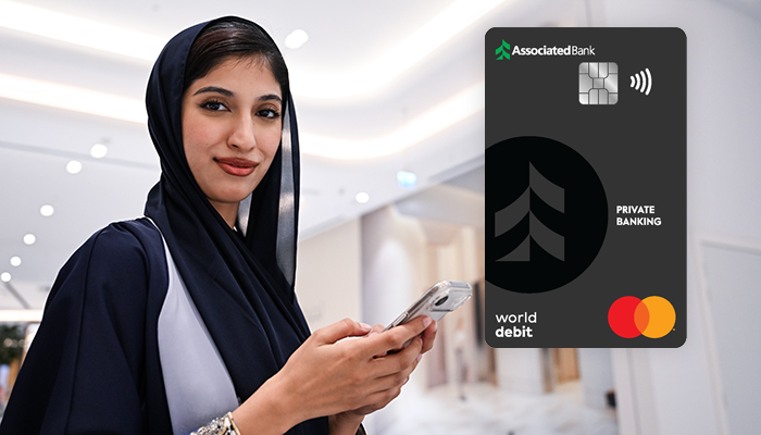 A woman looks at the camera while holding her phone. The Associated Bank Private Banking debit card is superimposed on the image.