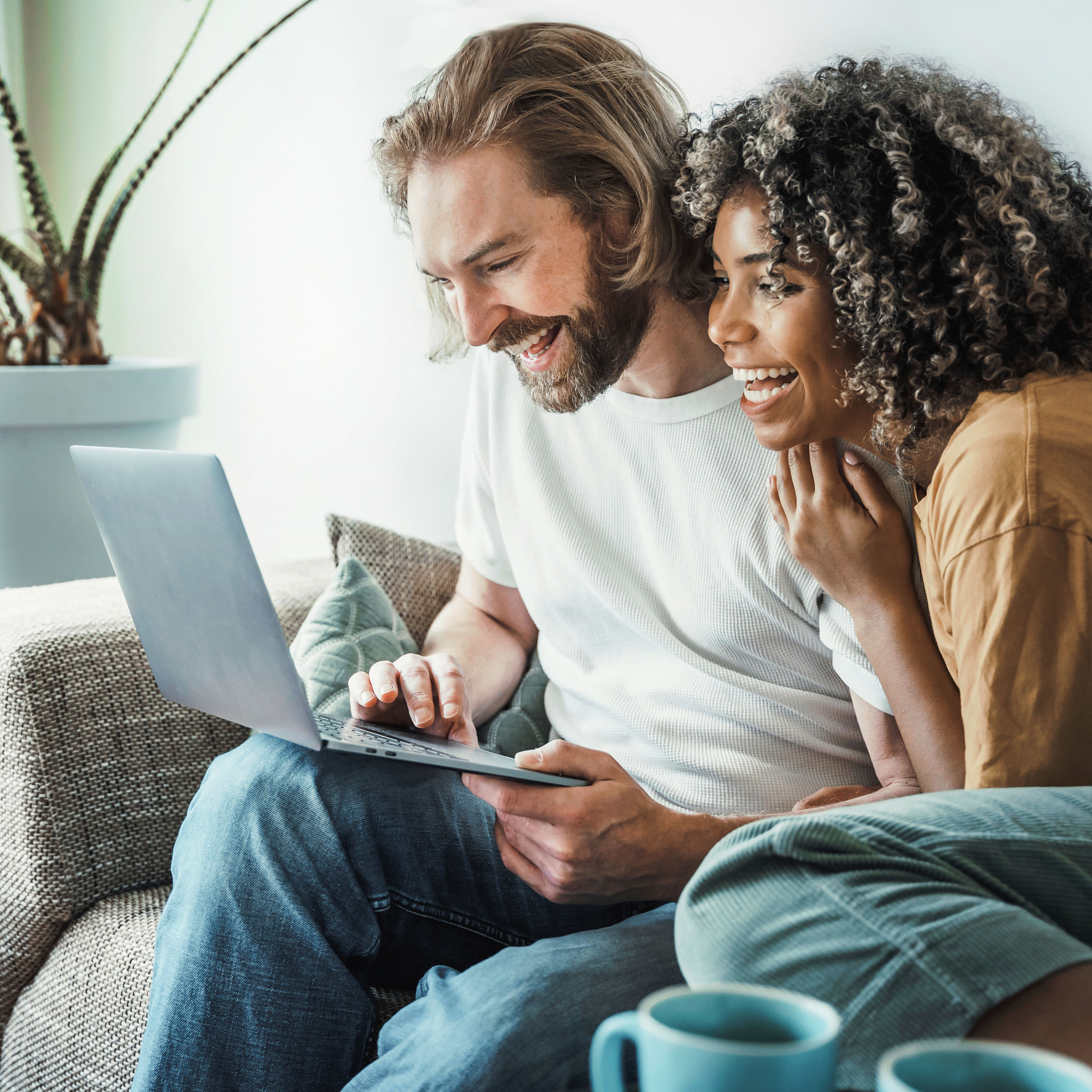 Multiracial young couple watching computer laptop sitting on the sofa at home